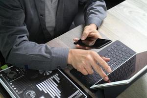 vista superior de la mano de un hombre de negocios usando un teléfono inteligente, compras en línea de pagos móviles, canal omni, computadora con teclado de acoplamiento de tableta digital, documentos, en una oficina moderna en un escritorio de madera foto