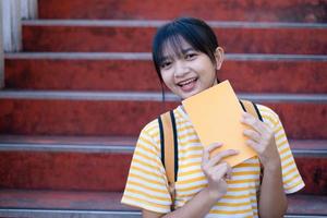 Student young girl hold yellow book sitting on stairs at school. photo