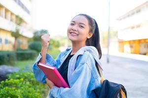 una estudiante feliz sostiene un libro y una mochila en la escuela, una chica asiática. foto