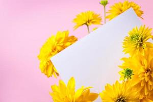 tarjeta de felicitación en blanco en ramo de flores de verano amarillas sobre fondo rosa. foto