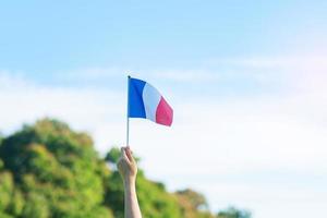 mano que sostiene la bandera de Francia sobre fondo de cielo azul. fiesta del día nacional francés, día de la bastilla y conceptos de celebración feliz foto