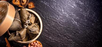 Close up, copy space, top view, flat lay. Famous asian chinese tasty handmade food in duan wu event, steamed rice dumplings shaped like pyramidal ingredient on black slate photo