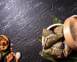 Close up, copy space, top view, flat lay. Famous asian chinese tasty handmade food in duan wu event, steamed rice dumplings shaped like pyramidal ingredient on black slate photo