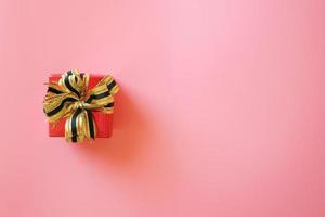 caja de regalo roja con cinta aislada en fondo rosa para regalar en vacaciones con espacio para copiar texto. vacaciones, presente, dando concepto. día de año nuevo, día de navidad, día de año nuevo chino, cumpleaños. foto