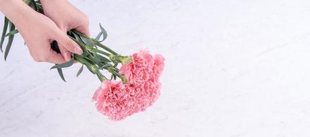 Design concept - Woman giving carnations bouquet on marble white background, top view, copy space, close up, mock up. Mothers day idea inspiration. photo