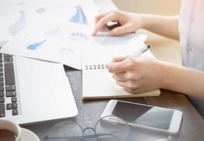 Business concept. Woman takes note for project with laptop and report in office desk. Backlighting, sun glare effect, close up, side view, copy space photo