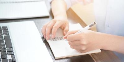 Business concept. Woman takes note for project with laptop and report in office desk. Backlighting, sun glare effect, close up, side view, copy space photo