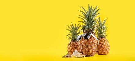 piña creativa mirando hacia arriba con gafas de sol y caparazón aislado en fondo amarillo, patrón de diseño de idea de playa de vacaciones de verano, espacio de copia de cerca foto