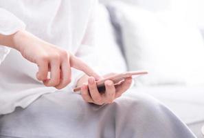 Side view of asia young woman in white sitting on sofa and using smart phone in bright living room, copy space, close up, blank for design concept photo