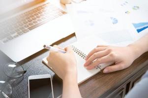 Business concept. Woman takes note for project with laptop and report in office desk. Backlighting, sun glare effect, close up, side view, copy space photo