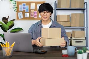 Empresario asiático, pyme, emprendedor o autónomo que trabaja en una caja de cartón, prepara la caja de entrega para el cliente, la venta en línea, el comercio electrónico, el embalaje y el concepto de envío. foto