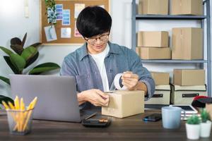 Empresario asiático, pyme, emprendedor o autónomo que trabaja en una caja de cartón, prepara la caja de entrega para el cliente, la venta en línea, el comercio electrónico, el embalaje y el concepto de envío. foto
