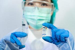 médico, científico, investigador mano en guantes azules o traje protector preparándose para ensayos de inyección clínica en humanos vacunación covid-19 concepto de riesgo biológico de vacunación por coronavirus.