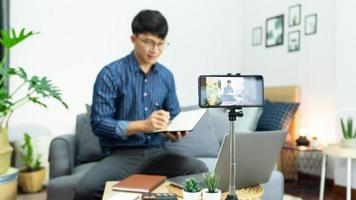 hombre asiático influyente en línea grabando video en vivo, usando una cámara de teléfono inteligente digital presenta una revisión del producto para el tema sobre el enfoque de blogs de video en la pantalla de la cámara en las redes sociales.