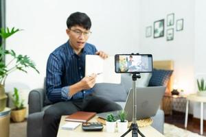 joven bloguero asiático grabando video vlog en la revisión de la cámara del producto en la oficina en casa, concéntrese en la pantalla de la cámara montada en trípode transmitiendo video en vivo a una red social.