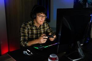 Involucró a un jugador asiático de ciberdeporte concentrado jugando videojuegos en la computadora en la habitación oscura de la noche en casa, concepto de deporte y tecnología foto