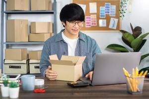 hombre asiático emprendedor emprendedor de pequeñas empresas pyme hombre independiente que trabaja con una caja para el embalaje de marketing en línea y la escena de entrega en la oficina en casa, concepto de vendedor de negocios en línea. foto