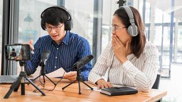 Asian Man and woman podcasters in headphones recording content with colleague talking to microphone and camera in broadcast studio together, communication technology and entertainment concept photo