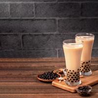 Delicious bubble milk tea with tapioca pearl ball in glass on wooden table and dark gray brick background, popular food and drink in Taiwan, close up