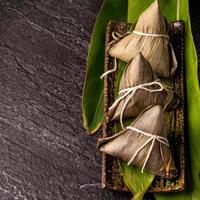 Close up, copy space, top view, flat lay. Famous asian chinese tasty handmade food in duan wu event, steamed rice dumplings shaped like pyramidal ingredient on black slate photo