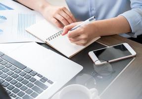 Business concept. Woman takes note for project with laptop and report in office desk. Backlighting, sun glare effect, close up, side view, copy space photo