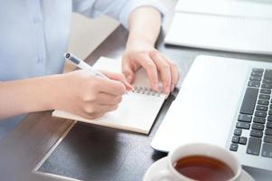 Business concept. Woman takes note for project with laptop and report in office desk. Backlighting, sun glare effect, close up, side view, copy space photo