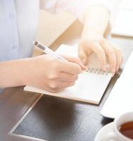 Business concept. Woman takes note for project with laptop and report in office desk. Backlighting, sun glare effect, close up, side view, copy space photo