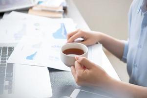 Business concept. Woman reading reports and drinking for rest in office table. Backlighting, sun glare effect, close up, side view, copy space photo