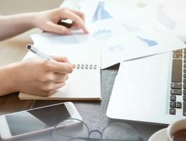 Business concept. Woman takes note for project with laptop and report in office desk. Backlighting, sun glare effect, close up, side view, copy space photo