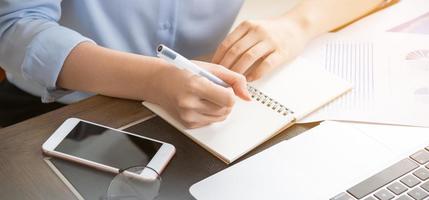 Business concept. Woman takes note for project with laptop and report in office desk. Backlighting, sun glare effect, close up, side view, copy space photo