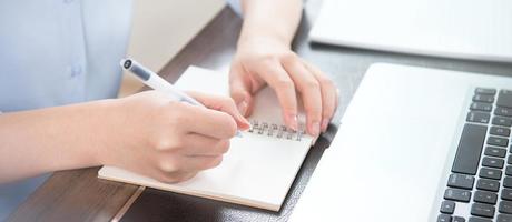 Business concept. Woman takes note for project with laptop and report in office desk. Backlighting, sun glare effect, close up, side view, copy space photo