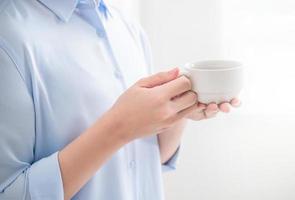 Side view of asia young business woman in blue shirt dress standing lying on the wall beside window in day life and drinking, copy space, close up photo