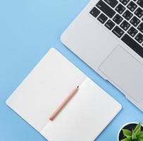 Girl write on open white book or accounting on a minimal clean light blue desk with laptop and accessories, copy space, flat lay, top view, mock up photo