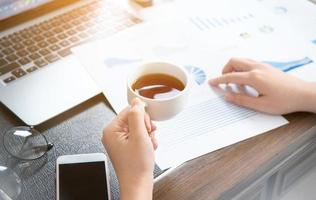 Business concept. Woman reading reports and drinking for rest in office table. Backlighting, sun glare effect, close up, side view, copy space photo