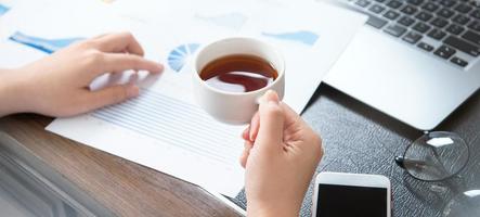 Business concept. Woman reading reports and drinking for rest in office table. Backlighting, sun glare effect, close up, side view, copy space photo