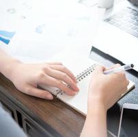Business concept. Woman takes note for project with laptop and report in office desk. Backlighting, sun glare effect, close up, side view, copy space photo