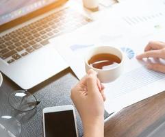 Business concept. Woman reading reports and drinking for rest in office table. Backlighting, sun glare effect, close up, side view, copy space photo