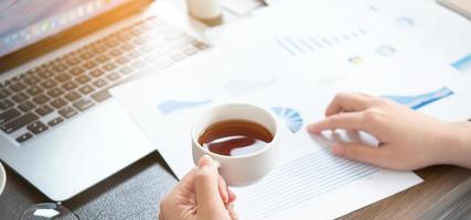 Business concept. Woman reading reports and drinking for rest in office table. Backlighting, sun glare effect, close up, side view, copy space photo