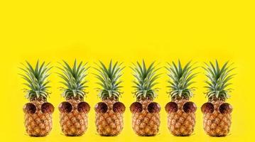 Creative pineapple looking up with sunglasses and shell isolated on yellow background, summer vacation beach idea design pattern, copy space close up photo