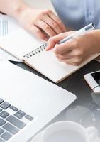 Business concept. Woman takes note for project with laptop and report in office desk. Backlighting, sun glare effect, close up, side view, copy space photo