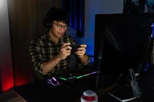 un apuesto y emocionado jugador asiático con auriculares disfruta y se regocija mientras juega videojuegos en una computadora en una habitación acogedora iluminada con luz cálida y de neón, juegos y tecnología concepto de deporte electrónico foto