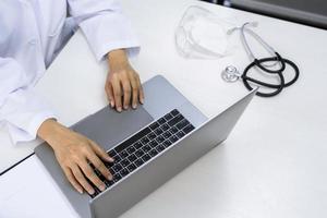 médico que trabaja con una computadora portátil sentada en el escritorio en la oficina o clínica del hospital, atención médica y concepto de tecnología médica.