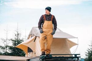 Adventurer man standing down on roof of the car with tent mounted on it for free travel camping lifestyle photo