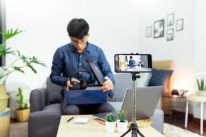 hombre asiático influyente en línea grabando video en vivo, usando una cámara de teléfono inteligente digital presenta una revisión del producto para el tema sobre el enfoque de blogs de video en la pantalla de la cámara en las redes sociales.