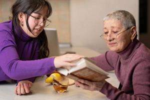 grandmother and granddaughter drink tea sitting at the table and read a book. photo