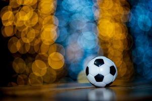 la pelota de fútbol blanca se coloca sobre un trozo de madera y tiene un hermoso fondo bokeh. foto