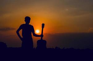 The silhouette of a guitarist who holds a guitar and has a sunset, silhouette concept. photo