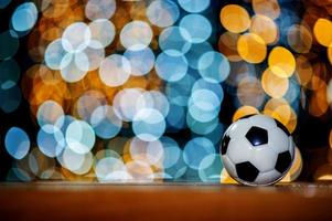 The white football ball is placed on a piece of wood and has a beautiful bokeh background. photo