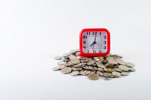 dinero, monedas de baht sobre un fondo blanco y un reloj rojo foto