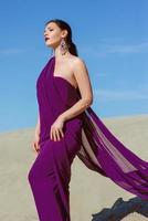 Amazing beautiful brunette woman with the Peacock feather in purple fabric in the desert. Oriental, indian, fashion, style concept photo